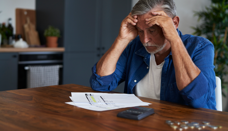 Elderly man surrounded by pills and a calculator, highlighting the significance of informed decisions to safeguard financial health. He is reflecting on the financial losses of not having a good hosting provider for his website.